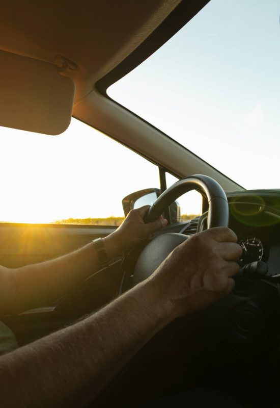 Man's hands holding with control the steering wheel of a car while driving on the road, traveling on vacation. Safe Transportation Adventure at Sunset